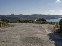 an empty gravel road winding down a hillside with green hills in the background and water on either side