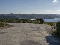 an empty gravel road winding down a hillside with green hills in the background and water on either side