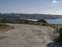 an empty gravel road winding down a hillside with green hills in the background and water on either side