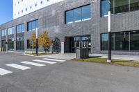 an empty grey parking lot next to a building with a window and metal trash can