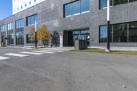 an empty grey parking lot next to a building with a window and metal trash can