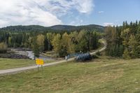 an empty highway surrounded by hills and pine trees, with an abandoned bridge leading to it