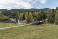 an empty highway surrounded by hills and pine trees, with an abandoned bridge leading to it