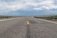 an empty highway with yellow line going through it and clouds in the background on either side of it