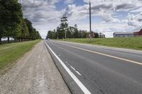 an empty highway with a barn in the back ground and a dirt bank on the other side