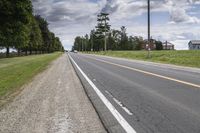 an empty highway with a barn in the back ground and a dirt bank on the other side