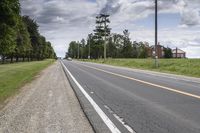 an empty highway with a barn in the back ground and a dirt bank on the other side