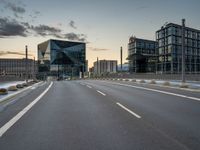 an empty highway leading into a big building with glass walls, and two others around it