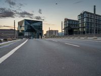 an empty highway leading into a big building with glass walls, and two others around it