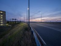 a long empty highway at twilight, with lights on at the side and in the distance