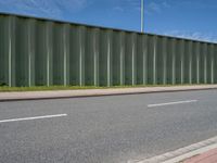 green metal fences line the side of an empty highway near a grassy field and white traffic light