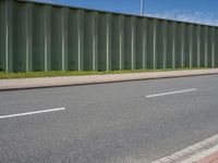 green metal fences line the side of an empty highway near a grassy field and white traffic light