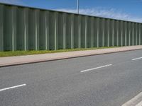 green metal fences line the side of an empty highway near a grassy field and white traffic light