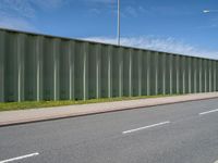 green metal fences line the side of an empty highway near a grassy field and white traffic light