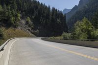 an empty highway in front of a mountainous valley surrounded by tall evergreens and hills