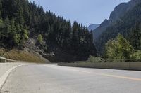 an empty highway in front of a mountainous valley surrounded by tall evergreens and hills