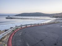 a empty highway near the ocean and a pier near the water's edge with a car on it