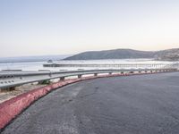 a empty highway near the ocean and a pier near the water's edge with a car on it