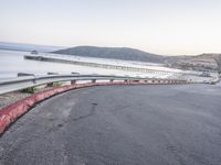 a empty highway near the ocean and a pier near the water's edge with a car on it