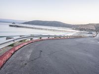 a empty highway near the ocean and a pier near the water's edge with a car on it