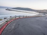 a empty highway near the ocean and a pier near the water's edge with a car on it