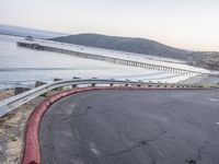 a empty highway near the ocean and a pier near the water's edge with a car on it