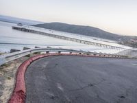 a empty highway near the ocean and a pier near the water's edge with a car on it