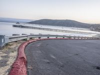 a empty highway near the ocean and a pier near the water's edge with a car on it