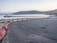 a empty highway near the ocean and a pier near the water's edge with a car on it