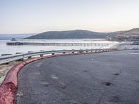 a empty highway near the ocean and a pier near the water's edge with a car on it