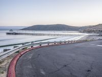 a empty highway near the ocean and a pier near the water's edge with a car on it