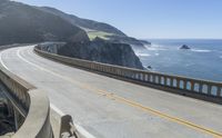 an empty highway leading to the ocean in california's pacific mountains, with cliffs in the distance