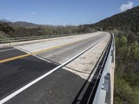 a view from a bridge overlooking trees and a mountain range of hills behind a bridge