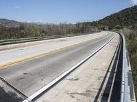 a view from a bridge overlooking trees and a mountain range of hills behind a bridge