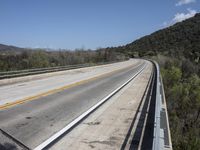 a view from a bridge overlooking trees and a mountain range of hills behind a bridge