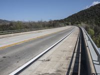 a view from a bridge overlooking trees and a mountain range of hills behind a bridge