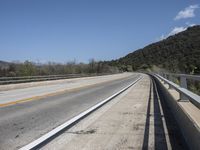 a view from a bridge overlooking trees and a mountain range of hills behind a bridge