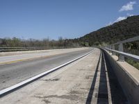 a view from a bridge overlooking trees and a mountain range of hills behind a bridge