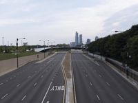 empty highway with skyscrapers in the distance in the background, and trees near the road