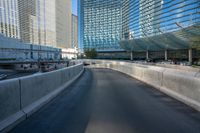 a paved empty highway passes by some large skyscrapers and large windows on either side