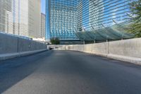 a paved empty highway passes by some large skyscrapers and large windows on either side