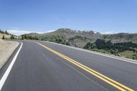 an empty highway surrounded by trees and a mountain range in the background in the distance