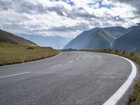 a empty highway curves toward the mountains on a cloudy day or summer day, with white lines painted along the left side