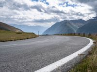 a empty highway curves toward the mountains on a cloudy day or summer day, with white lines painted along the left side