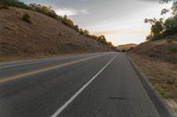 a motorcycle driving on a empty highway towards the horizon with hills in the background and a cloudy sky