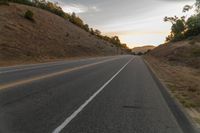 a motorcycle driving on a empty highway towards the horizon with hills in the background and a cloudy sky