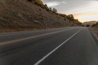 a motorcycle driving on a empty highway towards the horizon with hills in the background and a cloudy sky