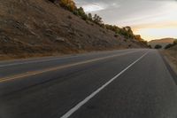 a motorcycle driving on a empty highway towards the horizon with hills in the background and a cloudy sky