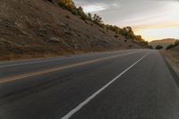 a motorcycle driving on a empty highway towards the horizon with hills in the background and a cloudy sky