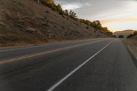 a motorcycle driving on a empty highway towards the horizon with hills in the background and a cloudy sky